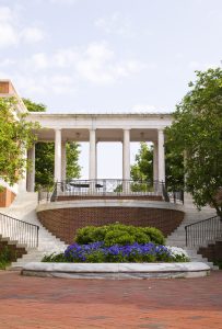 On the campus of Johns Hopkins University with foliage and blue and white flowers in a circular marble area with marble steps ascending on either side behind; marble columns are in background